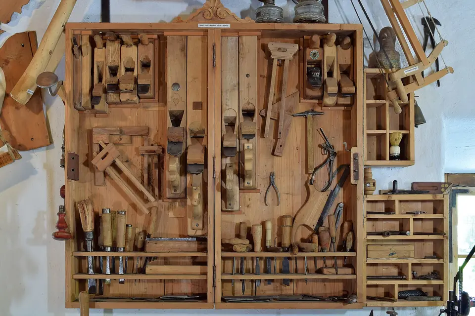 Armoire murale d'outils de menuisier où sont rangés rabots, ciseaux à bois, scies et serre-joints dans des casiers en bois.