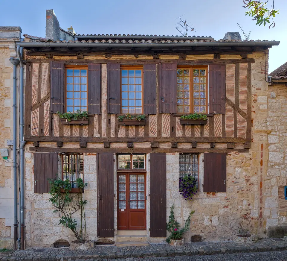 Maison à colombages de Bergerac avec fenêtres en bois, volets bruns, jardinières fleuries et porte d'entrée vitrée au rez-de-chaussée.