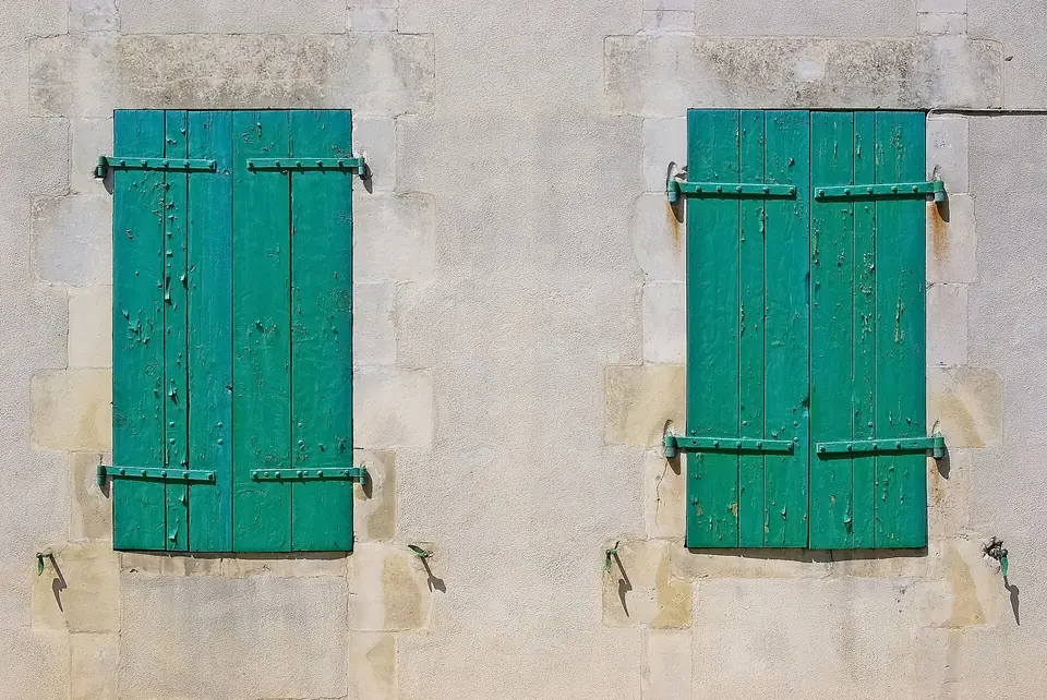 Deux paires de volets battants en bois peints en vert, fermés sur une façade enduite claire au Bois-Plage-en-Ré.